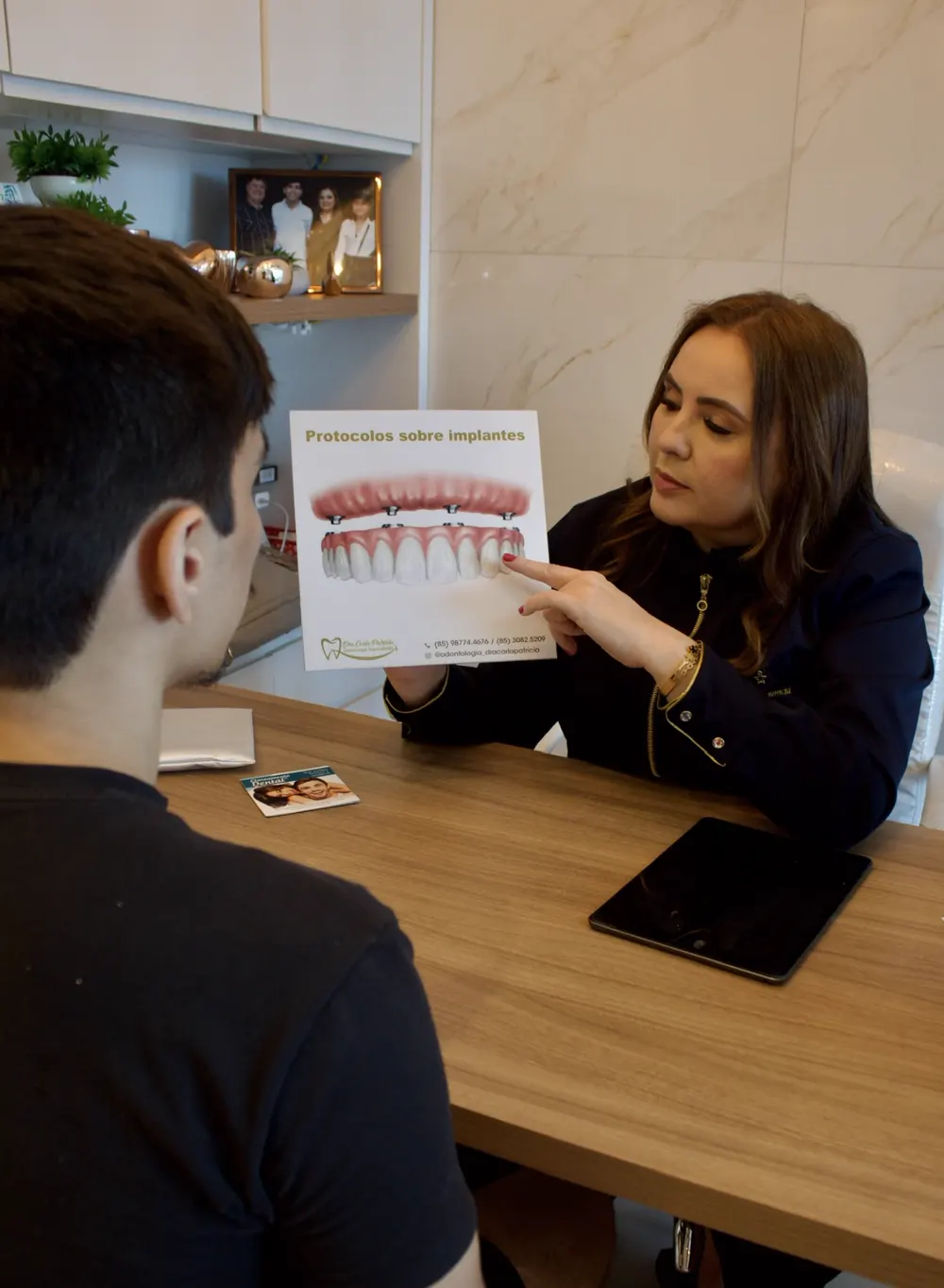 Dra. Carla Patrícia explicando um material sobre implantes para um paciente